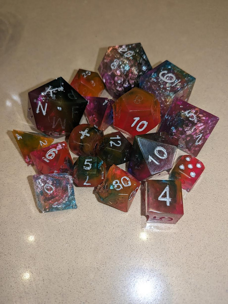 A pile of hand-poured resin polyhedral dice in jewel tones